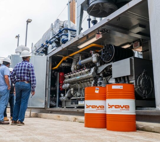 Men standing next to industrial oil drums and industrial engine