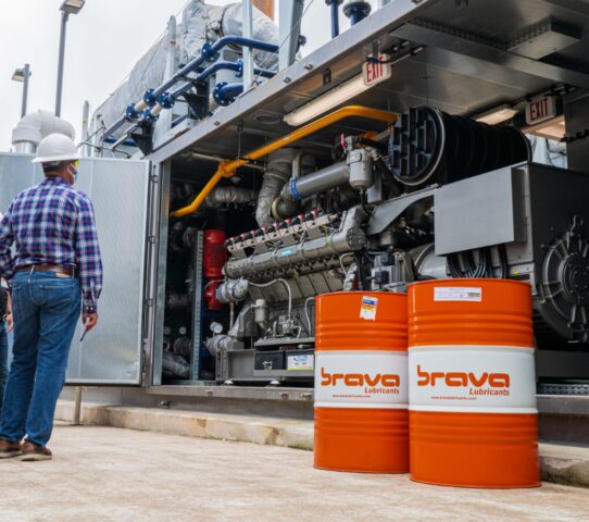 men looking at an industrial engine standing next to 2 drums of industrial oil