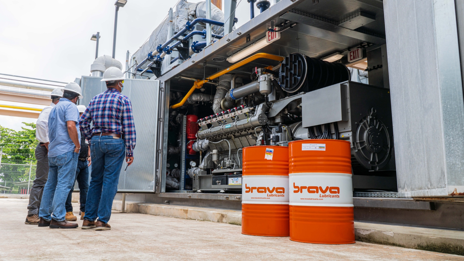 men looking at an industrial engine standing next to 2 drums of industrial oil